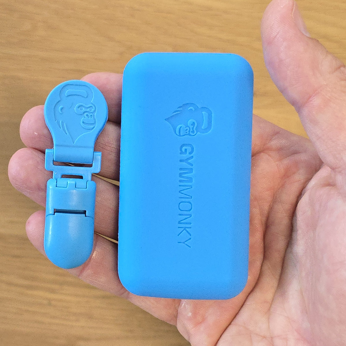 Hand holding the Magnetic Towel Clip and matching case, both embossed with the GYMMONKY monkey-head logo.