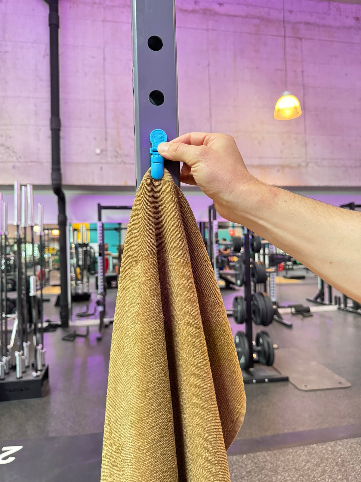 Hand befestigt ein Sporthandtuch mit dem GYMMONKY Magnetic Towel Clip am Stahl-Rack im Fitnessstudio