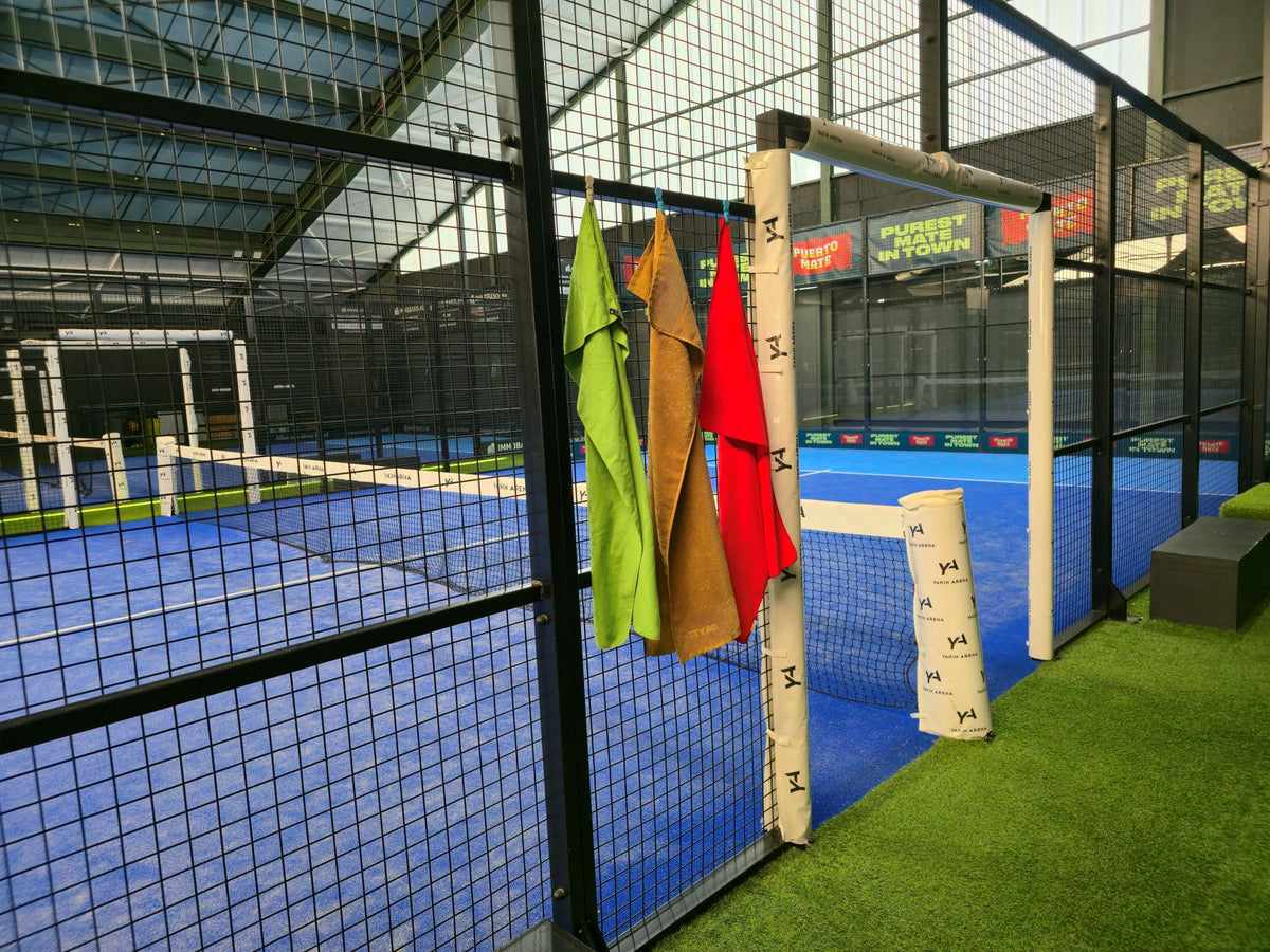 Drei Handtücher mit Magnetic Towel Clips am Gitter eines Padel Courts